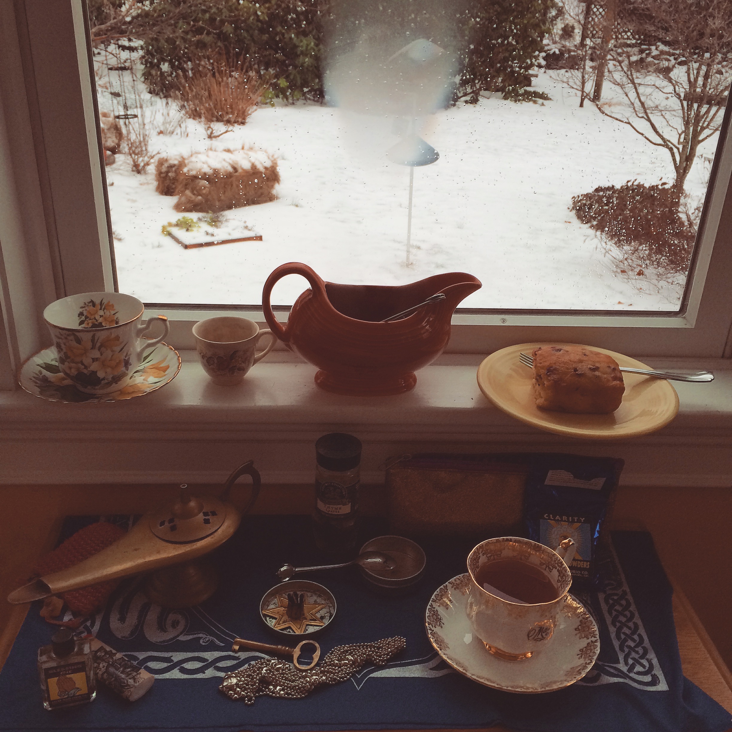 a windowsill altar with makeshift gravy boat teapot, food and drink offerings, and magical curios