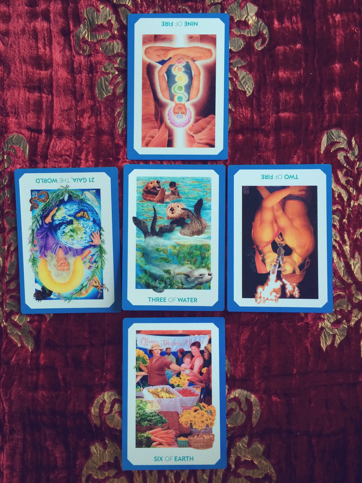 five tarot cards are laid on a red cloth with ornate gold designs upon it