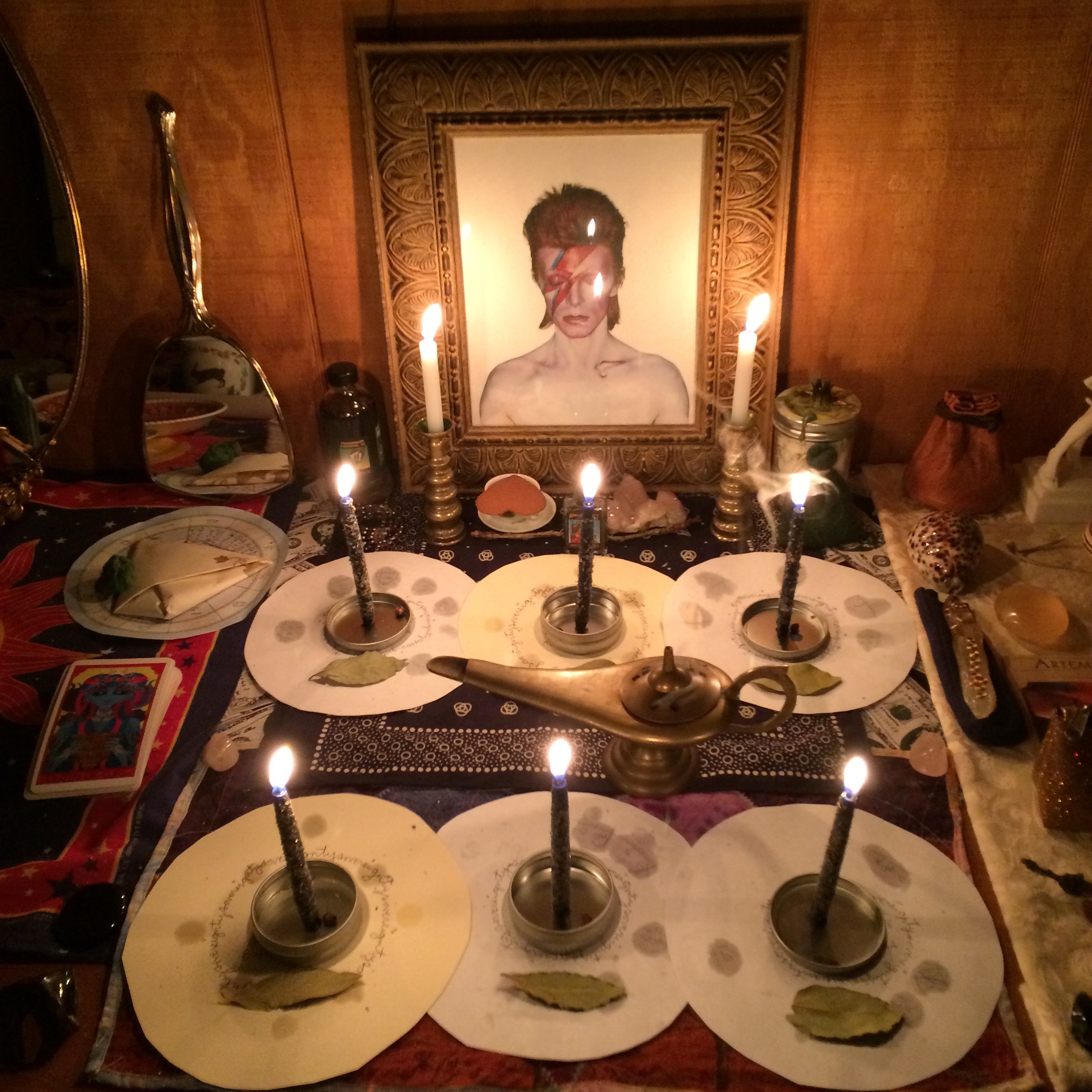 a frame picture of david bowie as aladdin sane with six small candles burning before it each on top of a round paper astrology chart