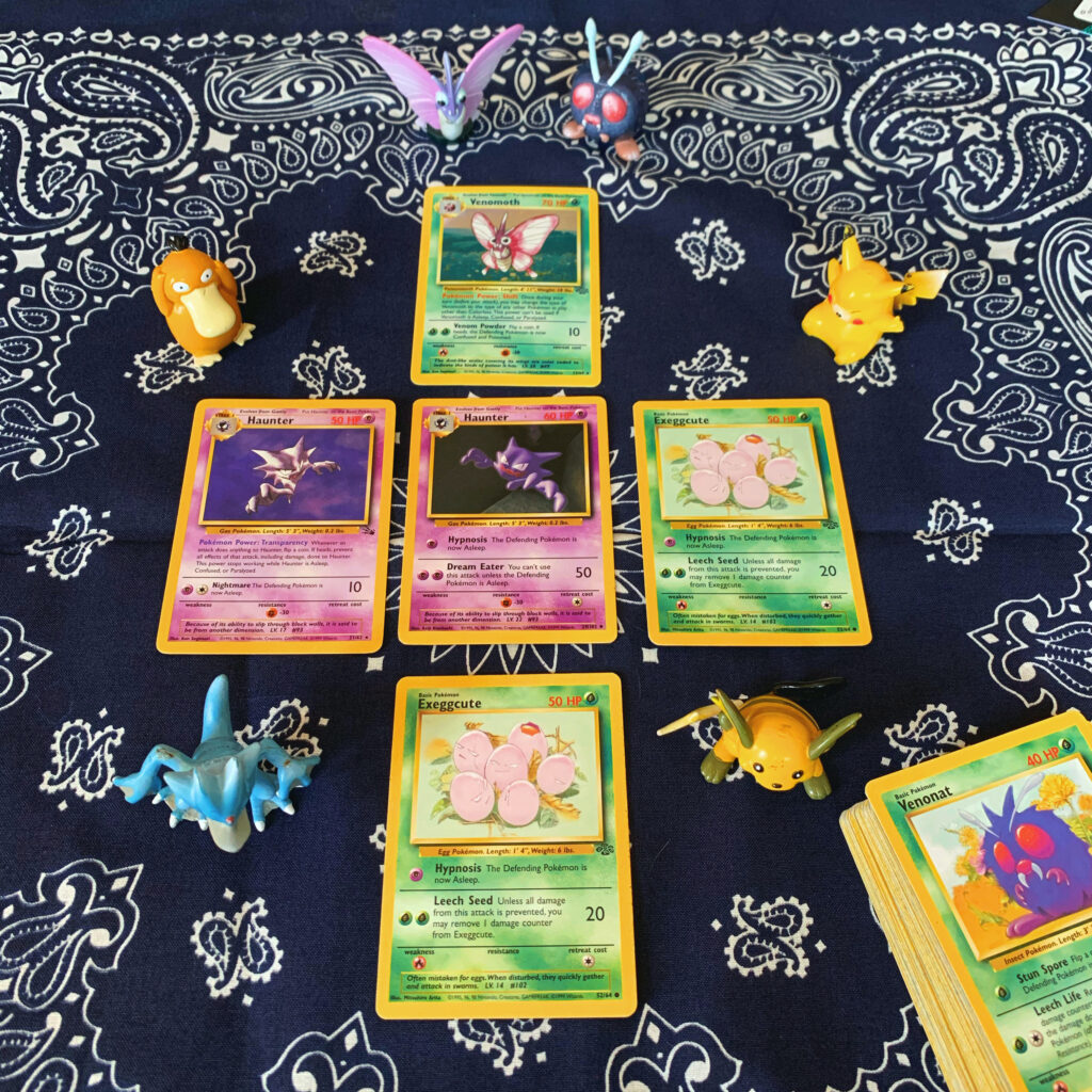 Photo of five Pokemon cards arranged in a tarot spread. On top is a holographic Venomoth card. Below are three cards in a row. From left to right: Haunter from the Fossil print, Haunter from the original print, and Exeggcute. Bottom row is another Exeggcute.